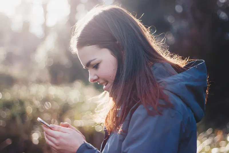 Mulher sorrindo enquanto conversa pelo celular ao ar livre