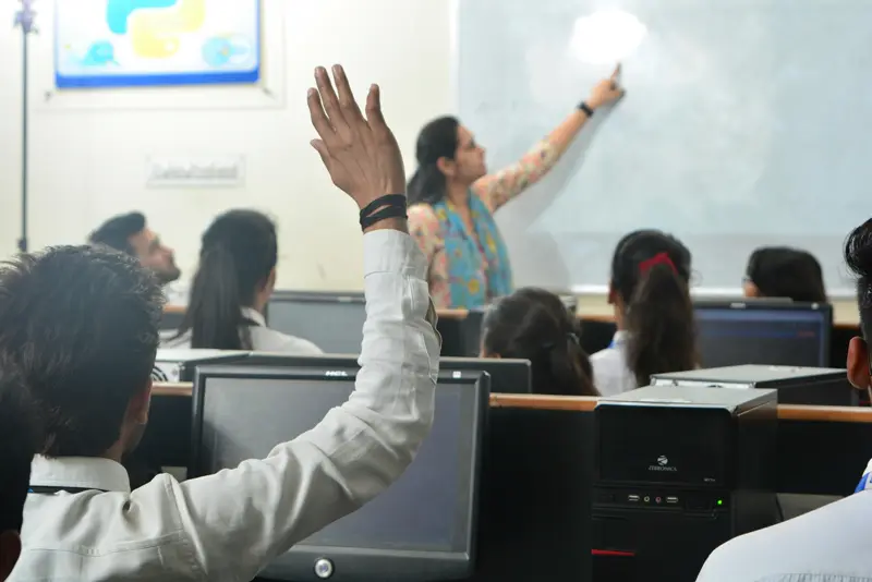 Professora dando aula para alunos numa sala com computadores