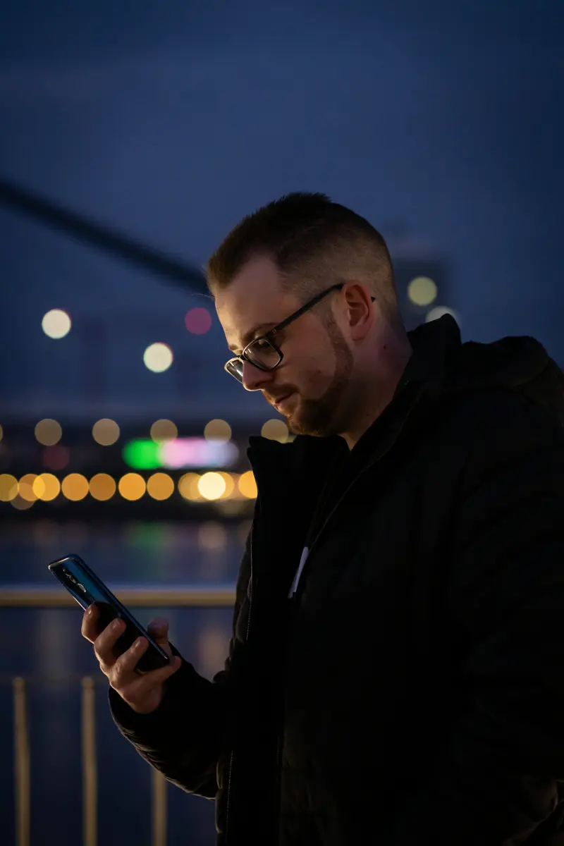 Homem de óculos usando o celular à noite na cidade